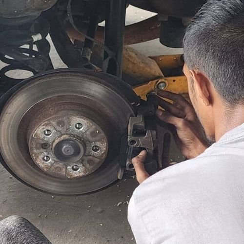 Mechanic working on a brake caliper beside an exposed brake disc.