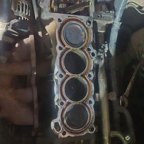 Engine block with the cylinder head removed, exposing four cylinders and pistons.