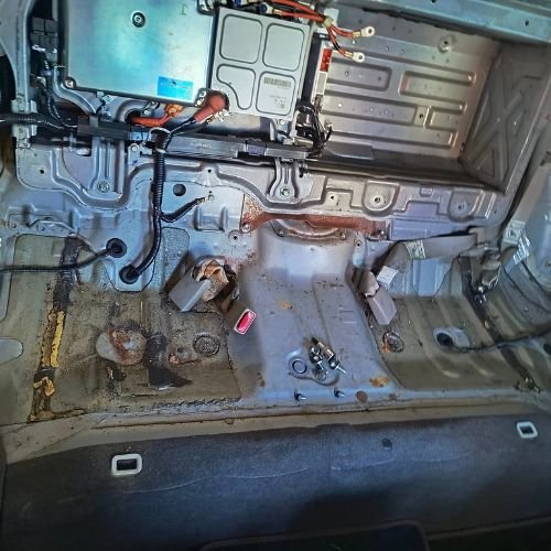 Exposed rear floor of a hybrid car with electrical components and wiring visible.