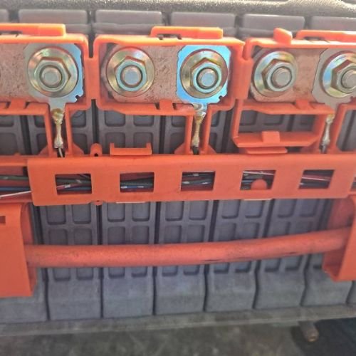 Close-up of hybrid battery terminals, copper connectors and orange protective covers.