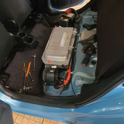 Hybrid battery unit exposed beneath the removed rear seat, with tools alongside.