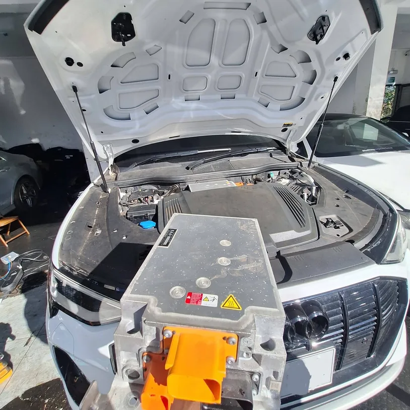Electronic module held in front of an Audi with its bonnet open.