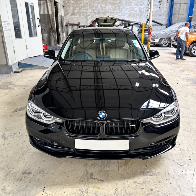 Front view of a glossy black BMW inside a workshop.