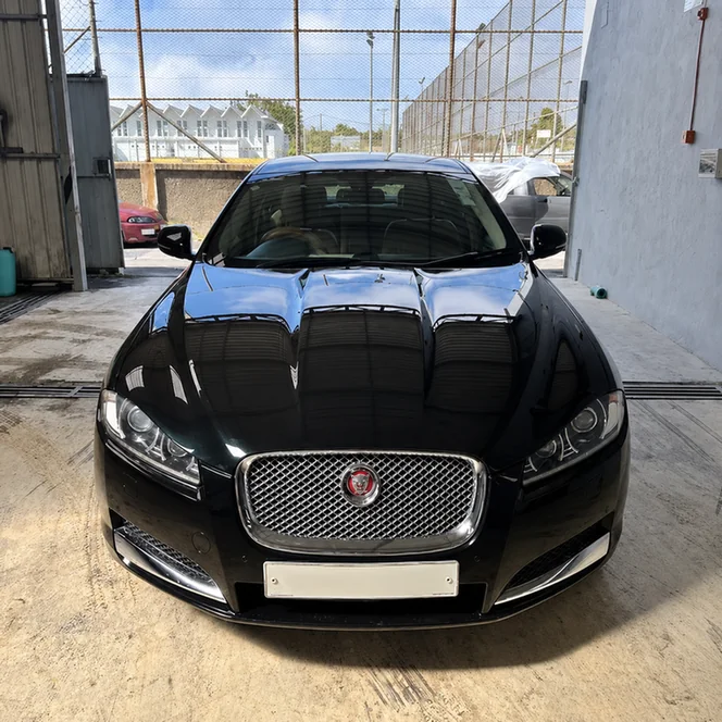 Front view of a black Jaguar with a chrome mesh grille inside a workshop.