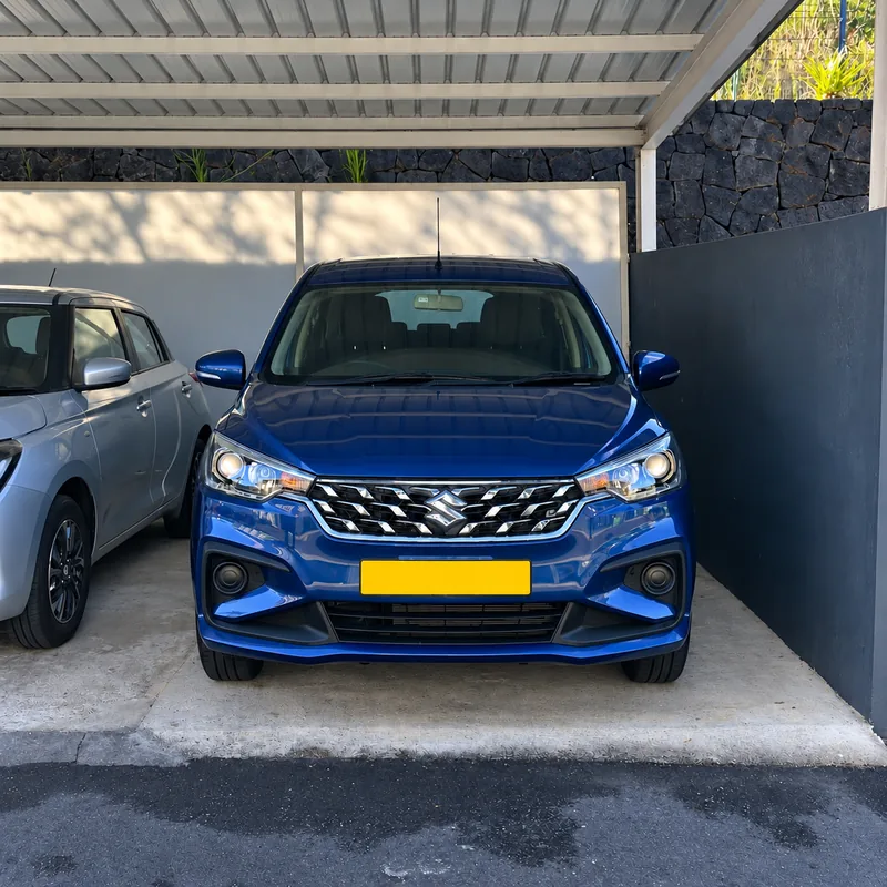 Blue Suzuki Ertiga parked under a covered carport with its headlights on.
