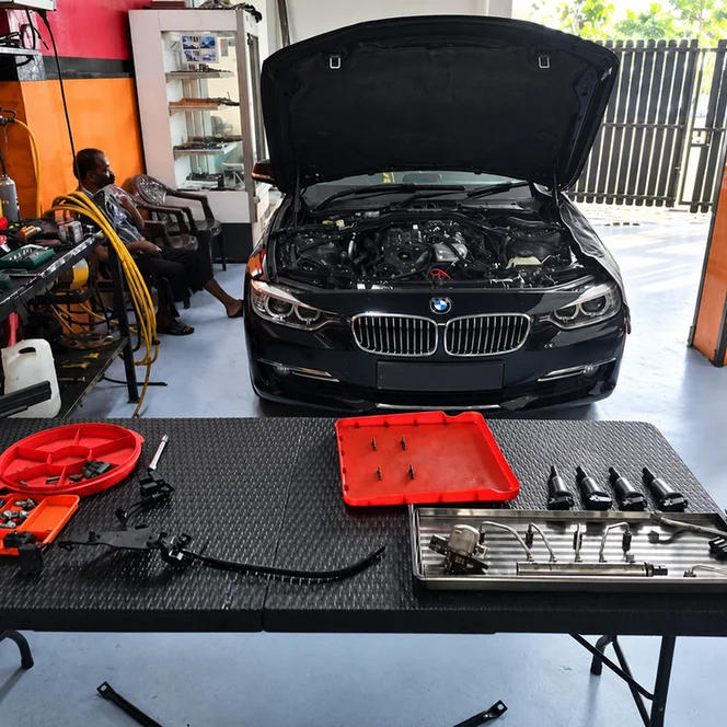 Black BMW 3 Series with its bonnet open and removed components arranged on a workbench.