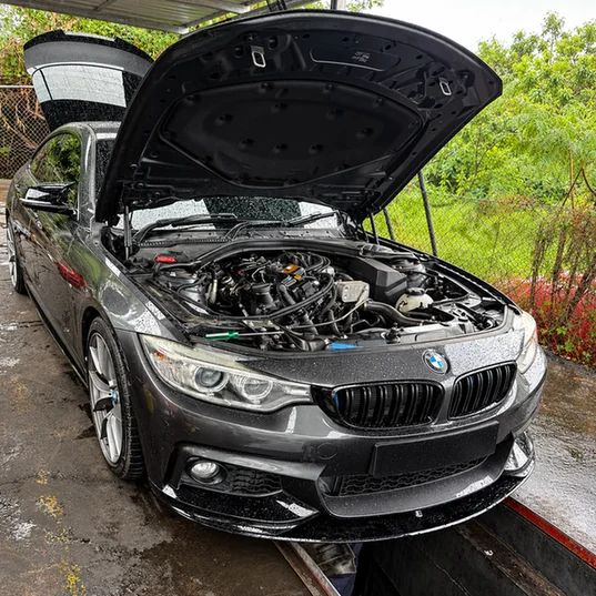 Grey BMW with its bonnet open and engine bay visible above an inspection pit.