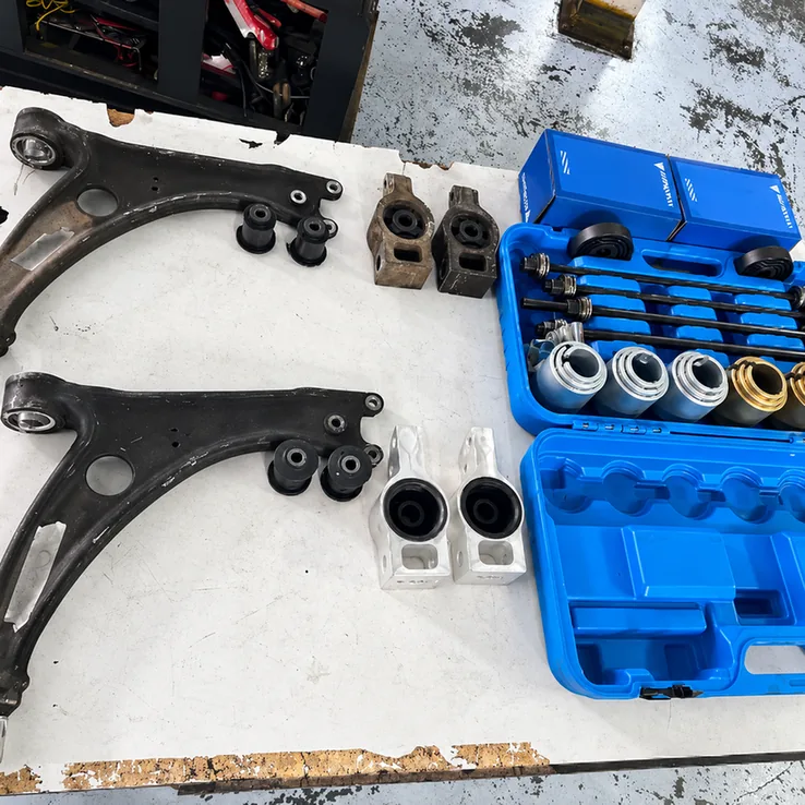 Control arms, suspension bushings and a bushing removal tool kit arranged on a workbench.