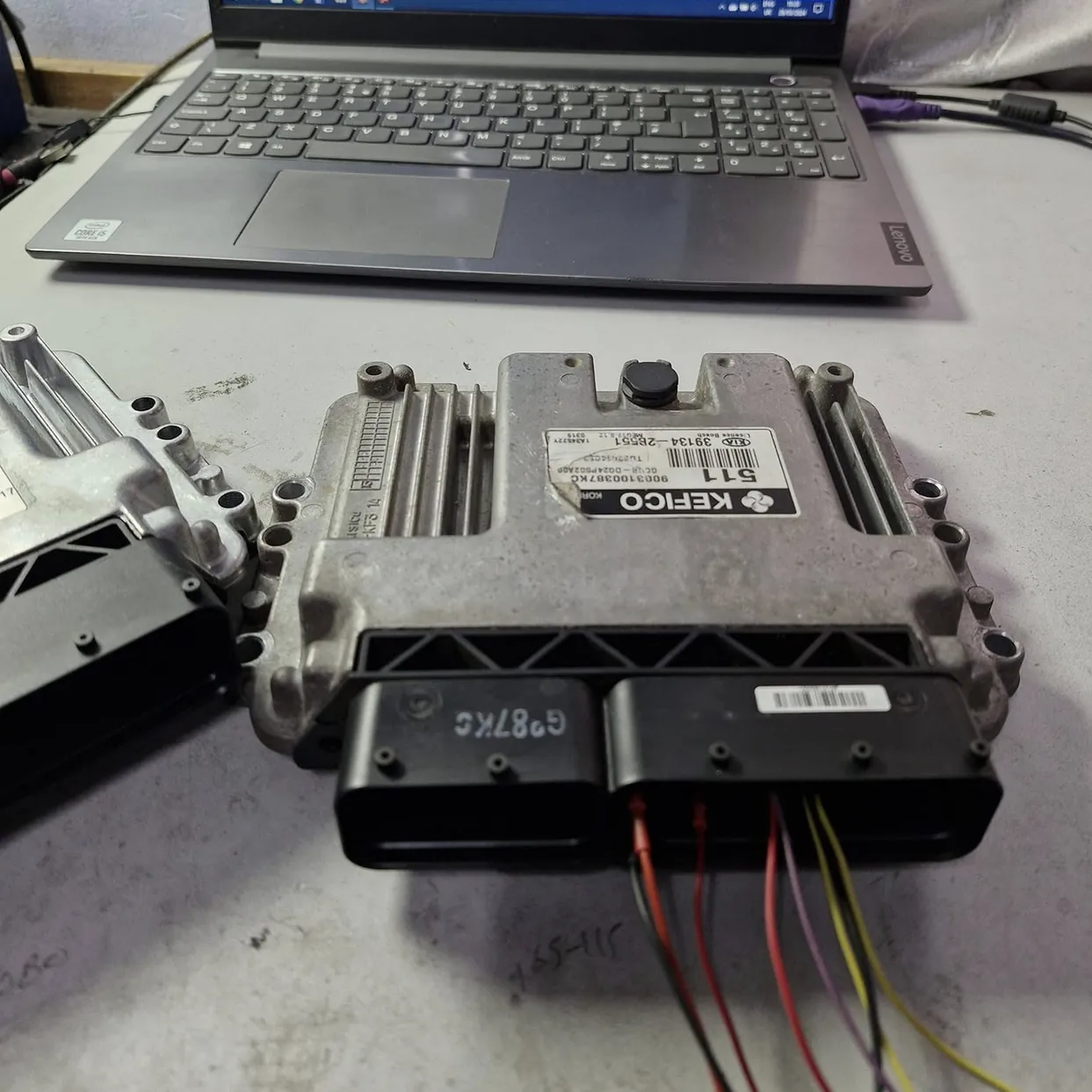 Car ECU connected to a laptop for programming on a workbench.