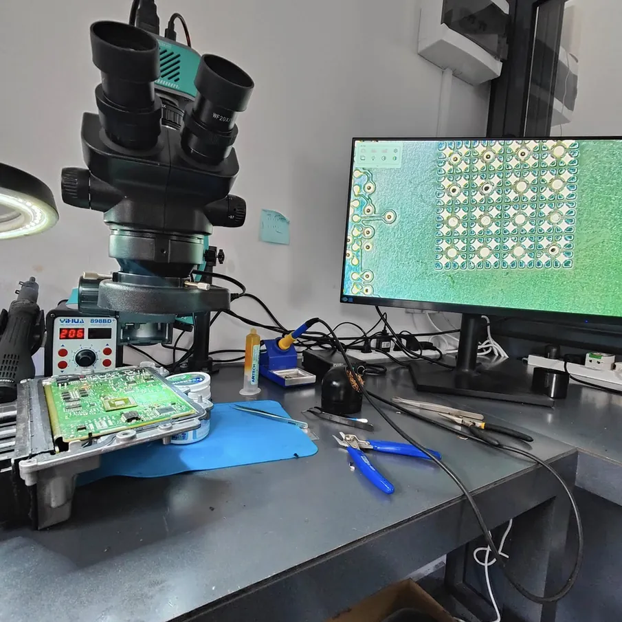 Automotive electronics workbench with a microscope, circuit board and inspection monitor.
