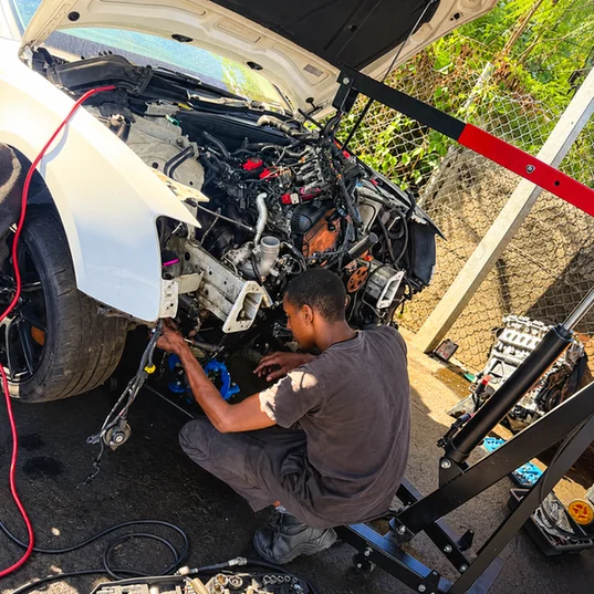 Mechanic working on an exposed engine beside an engine hoist.