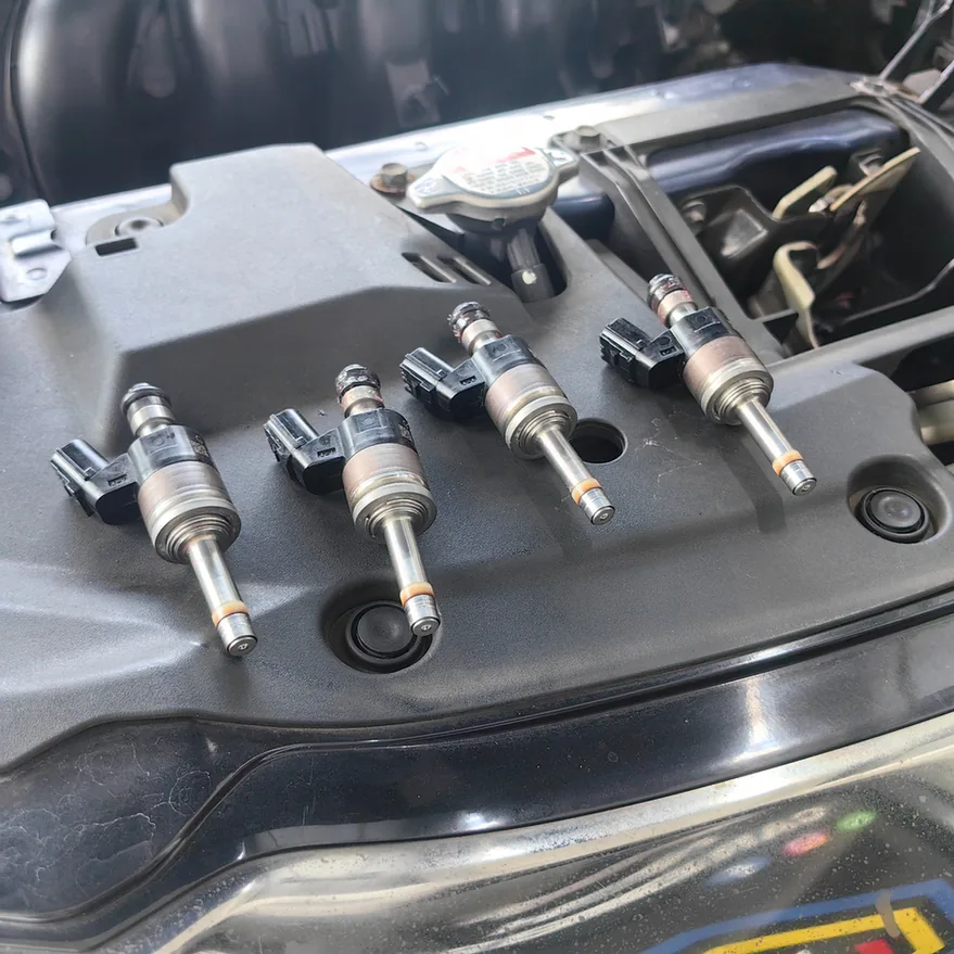 Four removed fuel injectors arranged on a car’s radiator cover.