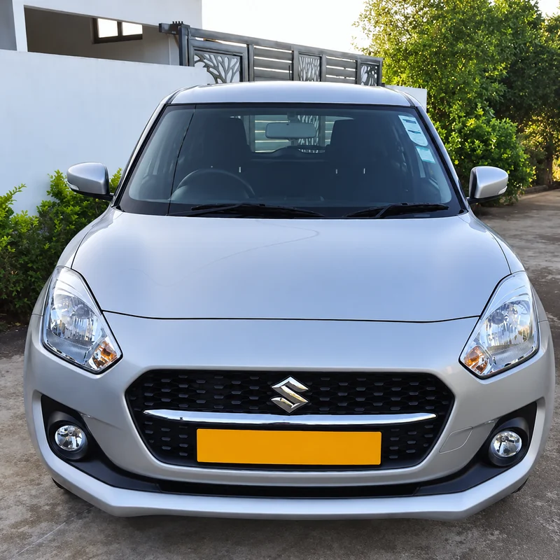 Front view of a grey Suzuki Swift parked outside beside a white wall.
