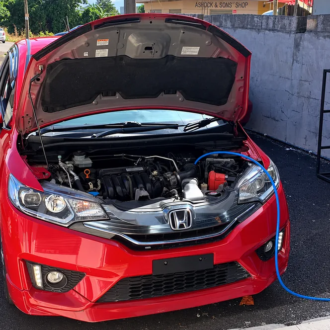 Red Honda Fit with its bonnet open and a blue service hose connected in the engine bay.