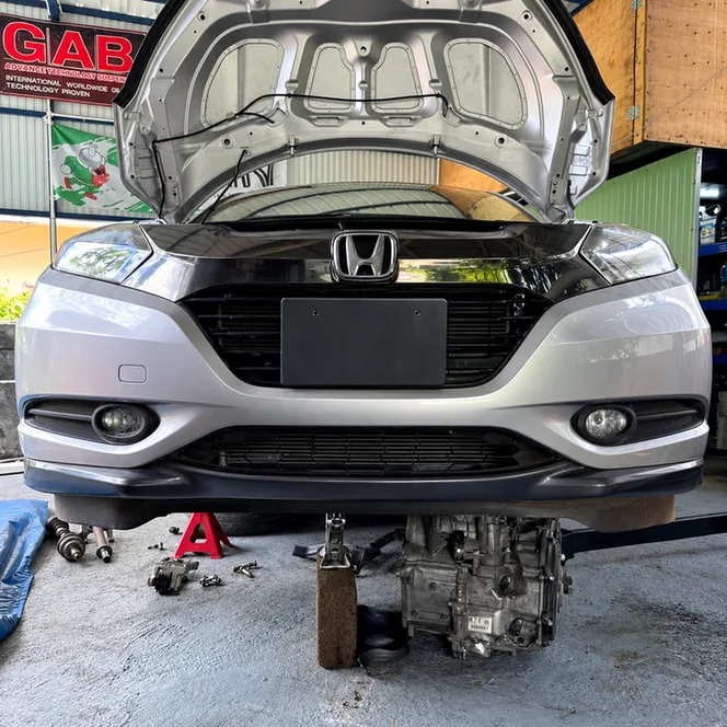 Silver Honda with its bonnet open and removed transmission beneath the front bumper.