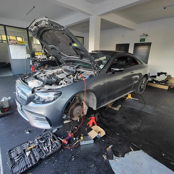 Mercedes-Benz in a workshop with its bonnet open and front wheel removed.