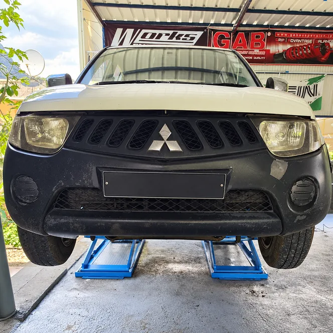 White Mitsubishi pickup raised on a blue workshop lift.