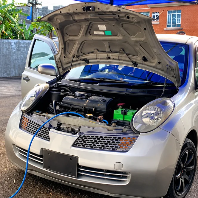 Silver Nissan March with its bonnet open and a blue service hose entering the engine bay.