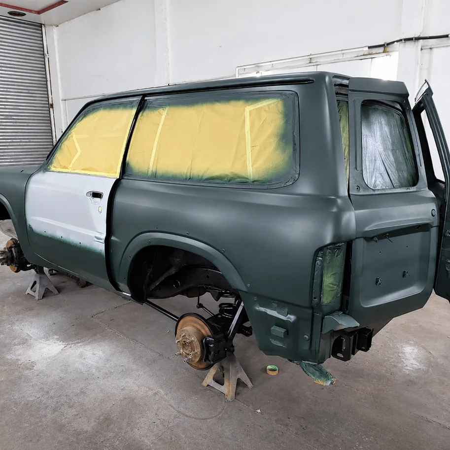Nissan Patrol on axle stands with masked windows and prepared body panels for painting.