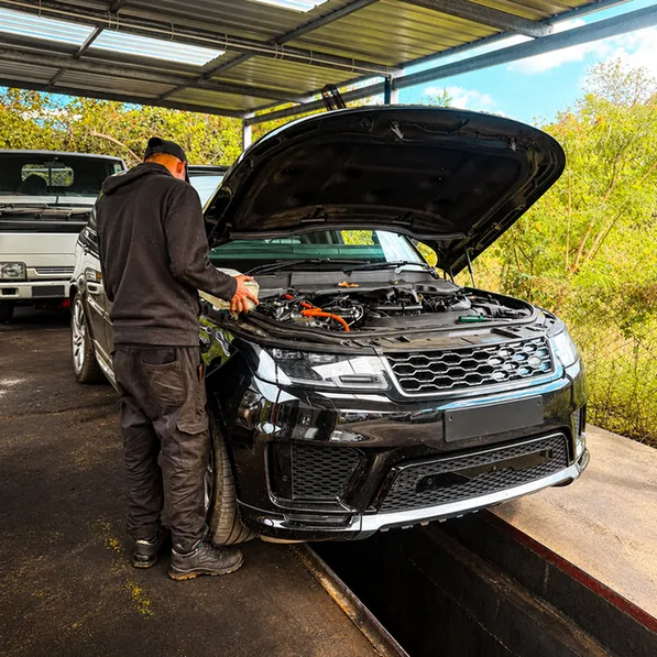 Mechanic working beside a black Range Rover with its bonnet open over an inspection pit.