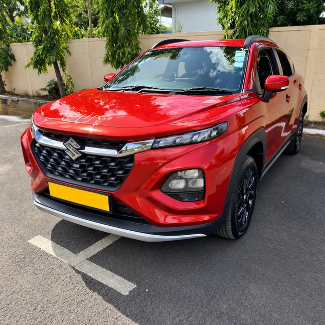Red Suzuki Fronx viewed from the front and side in an outdoor parking area.