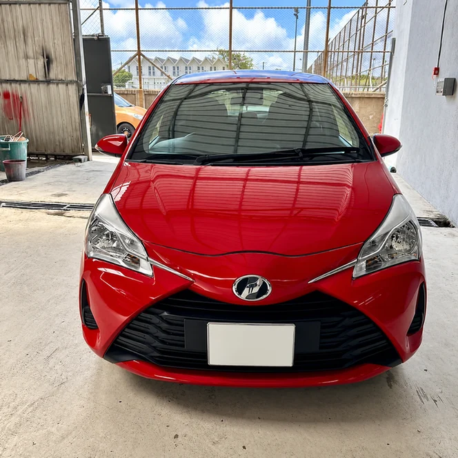 Front view of a red Toyota Vitz inside an automotive workshop.