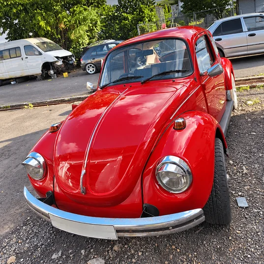 Classic red Volkswagen Beetle with chrome bumpers outside the workshop.