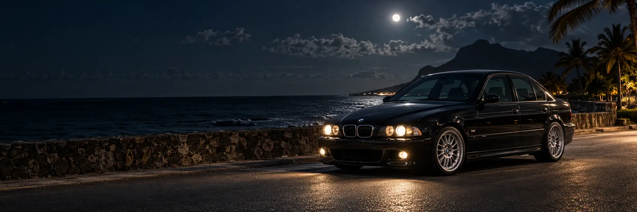 Black BMW M5 E39 parked beside a coastal road in Mauritius at night, with its headlights on.