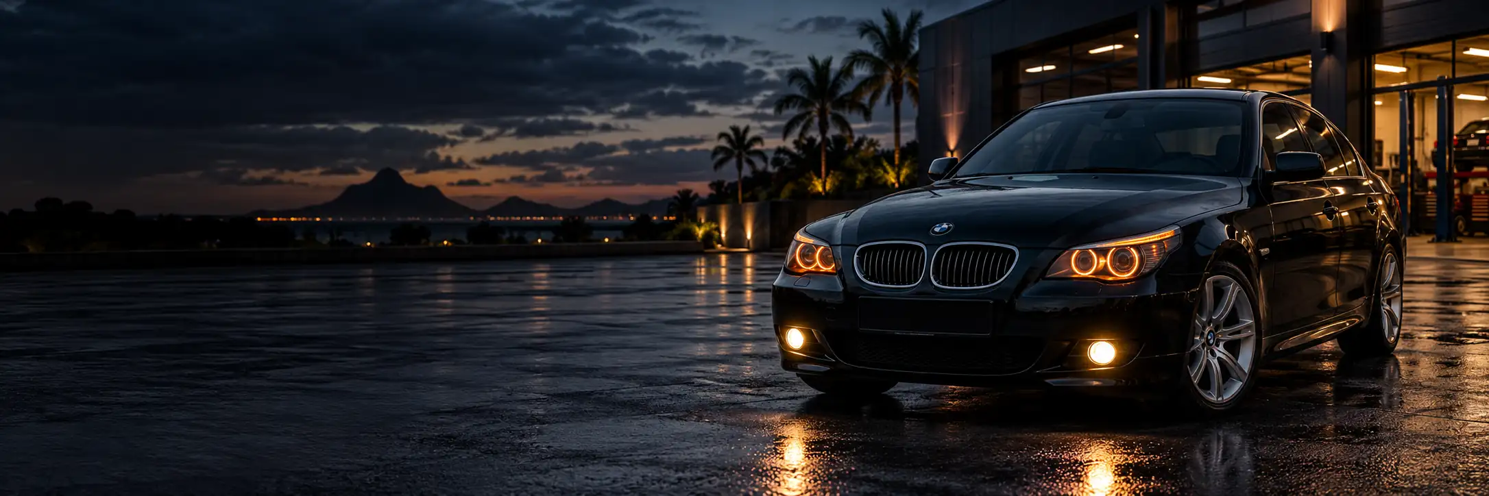 Black BMW E60 with orange halo headlights and illuminated fog lights beside a waterfront at dusk