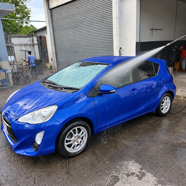 Blue Toyota Aqua being rinsed with a pressure washer outside the workshop.