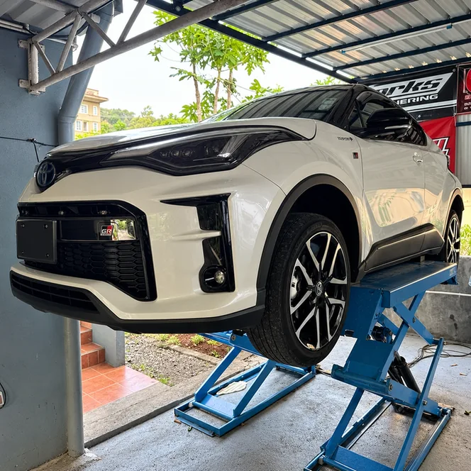 White Toyota C-HR hybrid raised on a blue scissor lift.