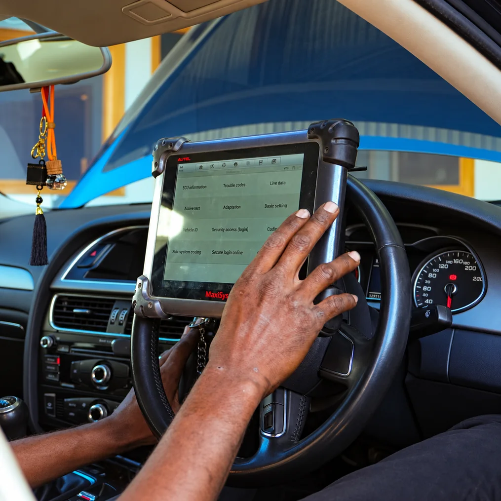 Technician using a diagnostic tablet inside a car with its bonnet open.