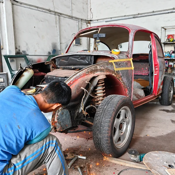 Technician working on the exposed front bodywork of a classic Volkswagen Beetle.