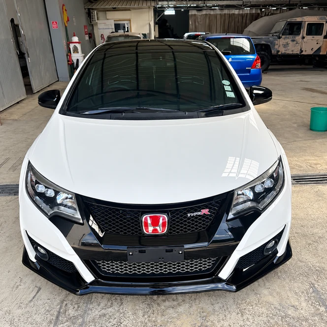 White Honda Civic with black front trim and a red Honda badge inside a workshop.